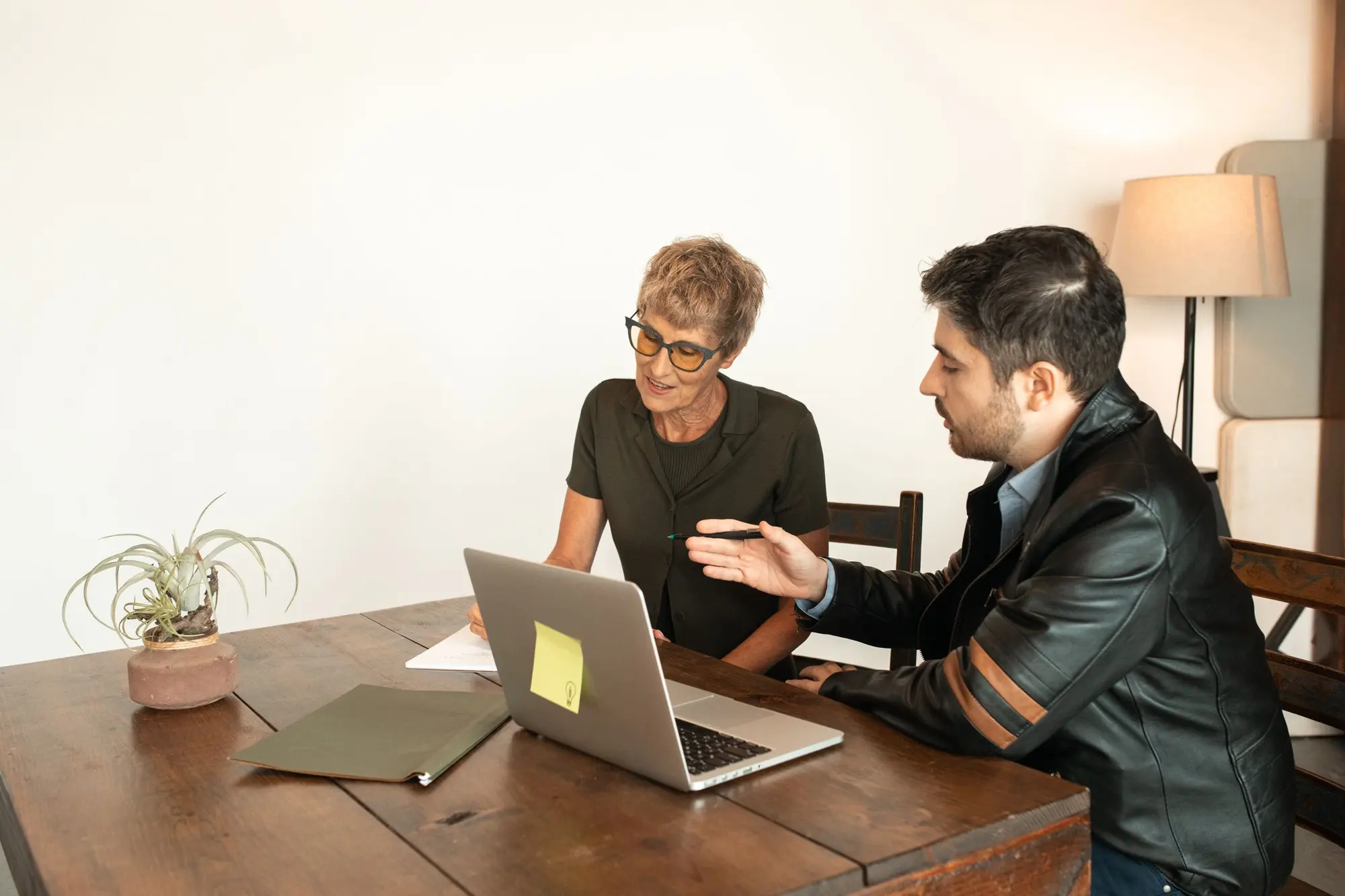 Two people reviewing plans together on a laptop at a wooden table