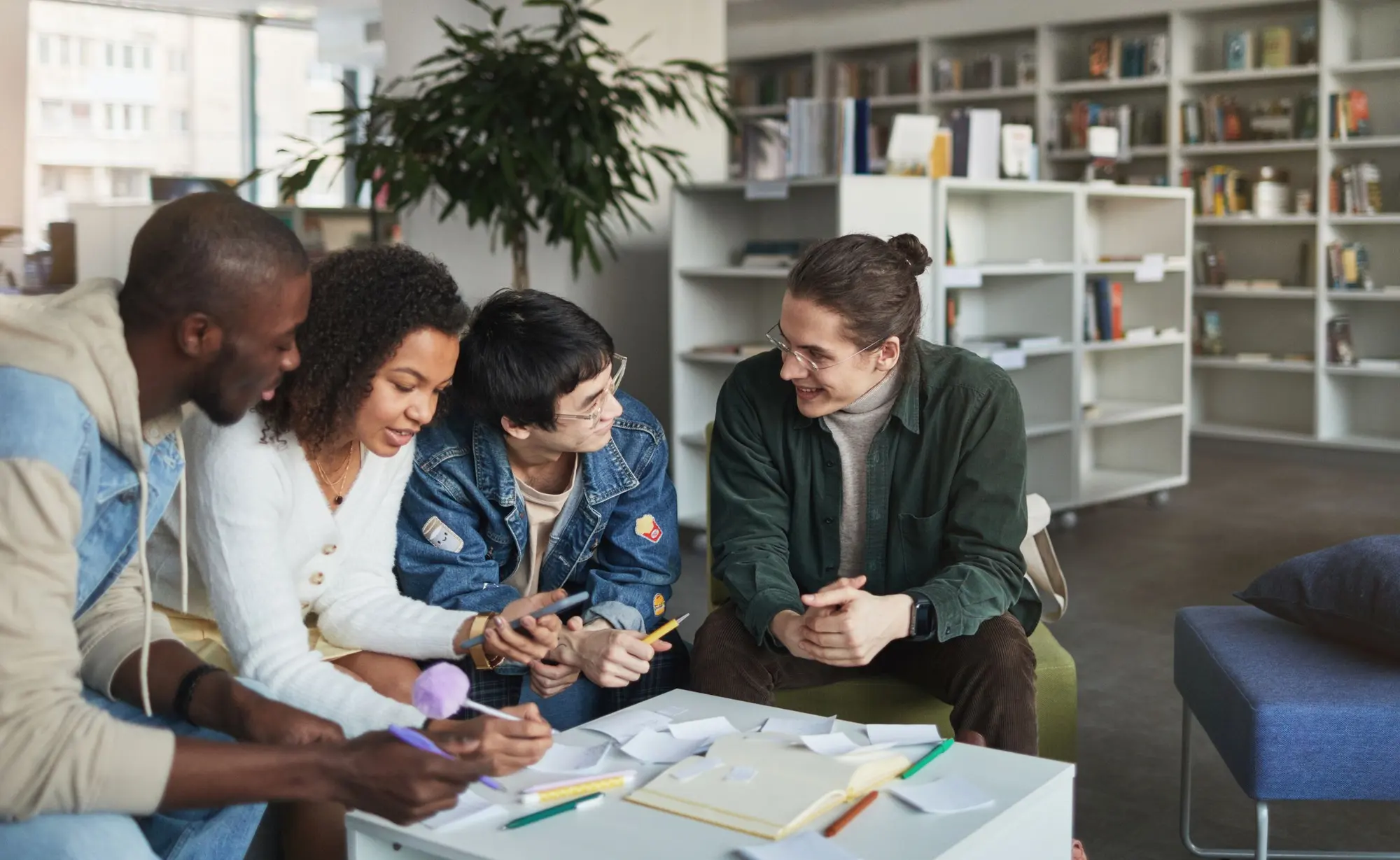 Four students talking over notes at a table in a library
